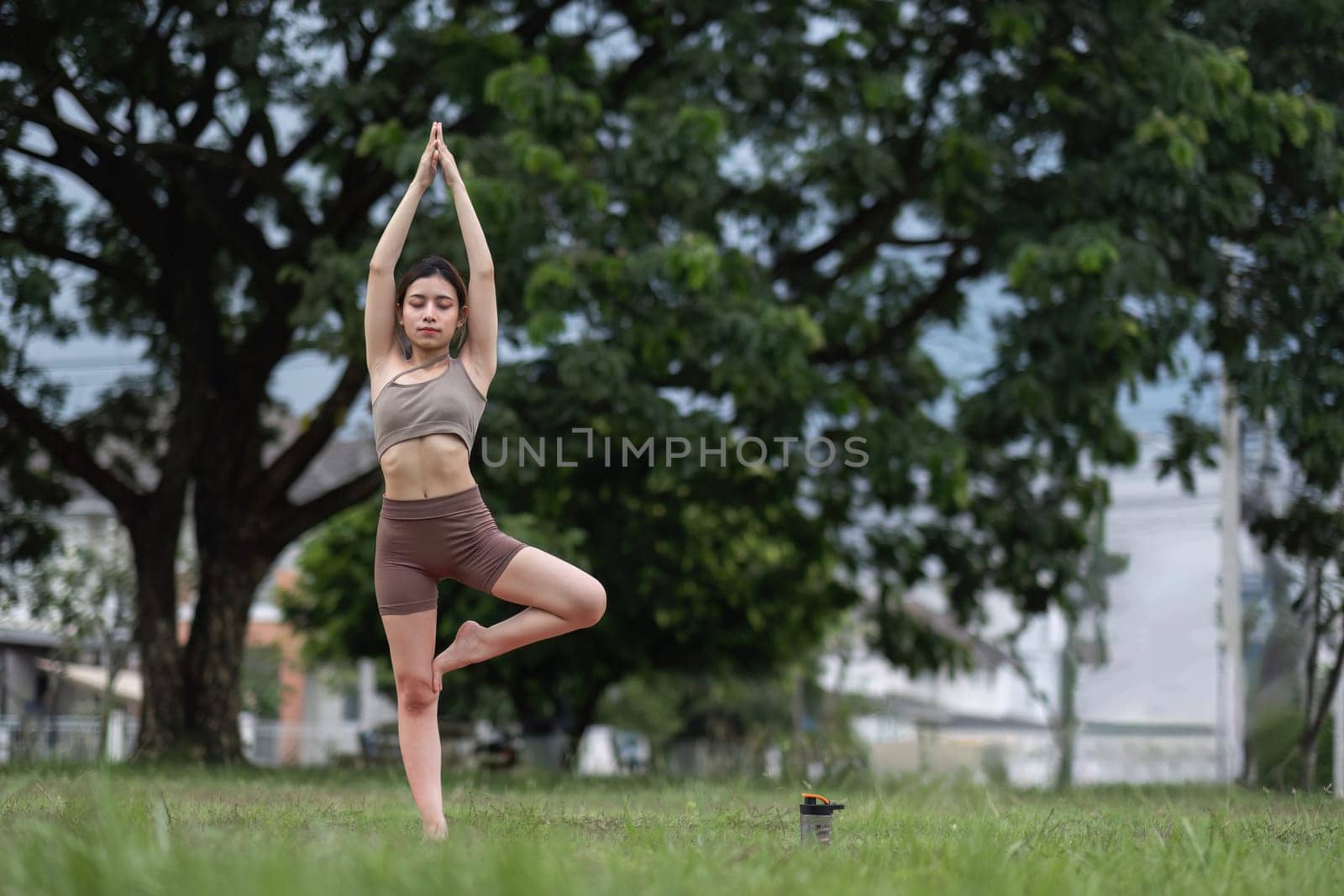 Young healthy Asian woman stretch her body on a yoga mat. Do yoga in a lush park Yoga and Pilates concept by wichayada