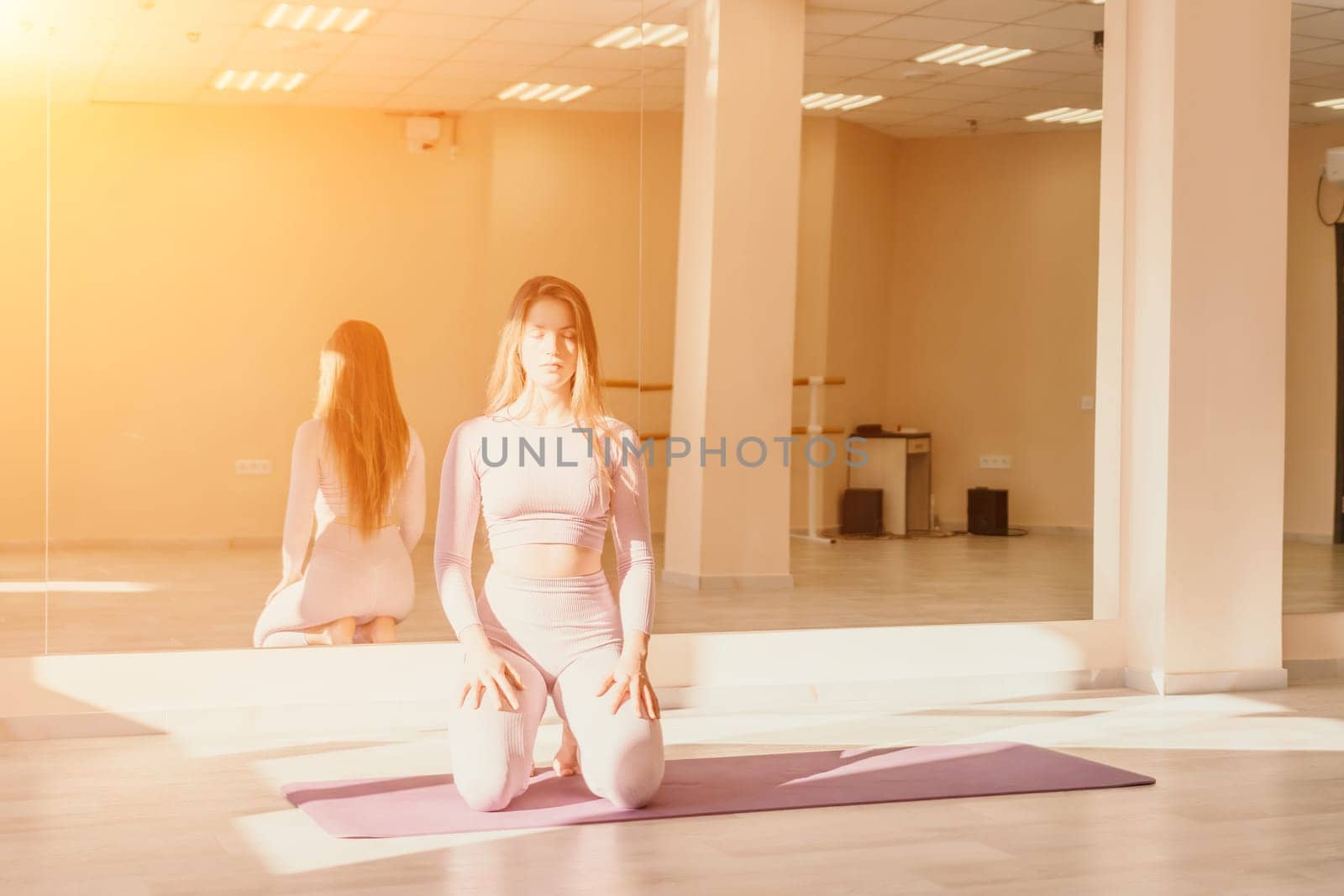 Young sporty woman, fitness instructor in pink sportswear doing stretching and pilates on yoga mat in the studio with mirror. Female fitness yoga routine concept. Healthy lifestyle and harmony. by panophotograph