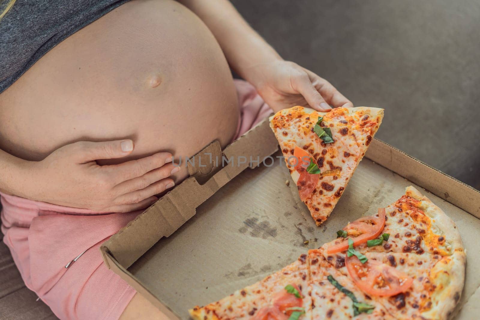 A pregnant woman enjoys a slice of pizza, savoring a moment of indulgence while satisfying her craving for a delightful, comforting treat. Excited Pregnant Young Lady Enjoying Pizza Holding Biting Tasty Slice Posing With Carton Box. Junk Food Lover Eating Italian Pizza. Unhealthy Nutrition Cheat Meal by galitskaya