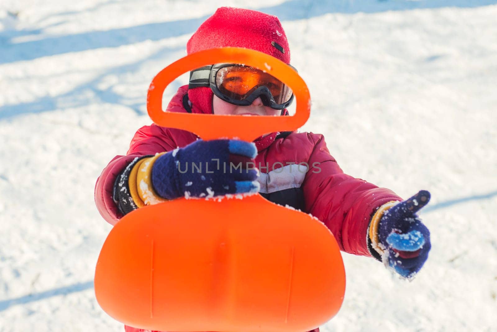 A boy is riding a sledge in snowy park in winter. Child outdoor activities.