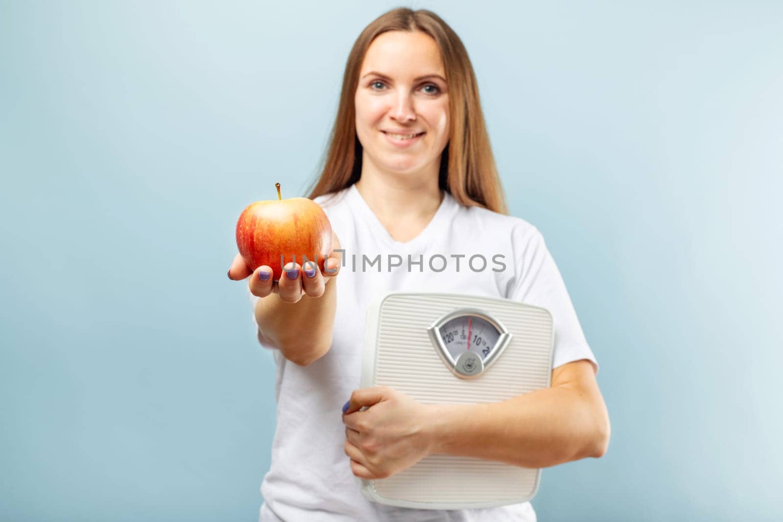Happy smiling woman holding weight scales and red apple on a blue background. Healthy eating concept. Diet