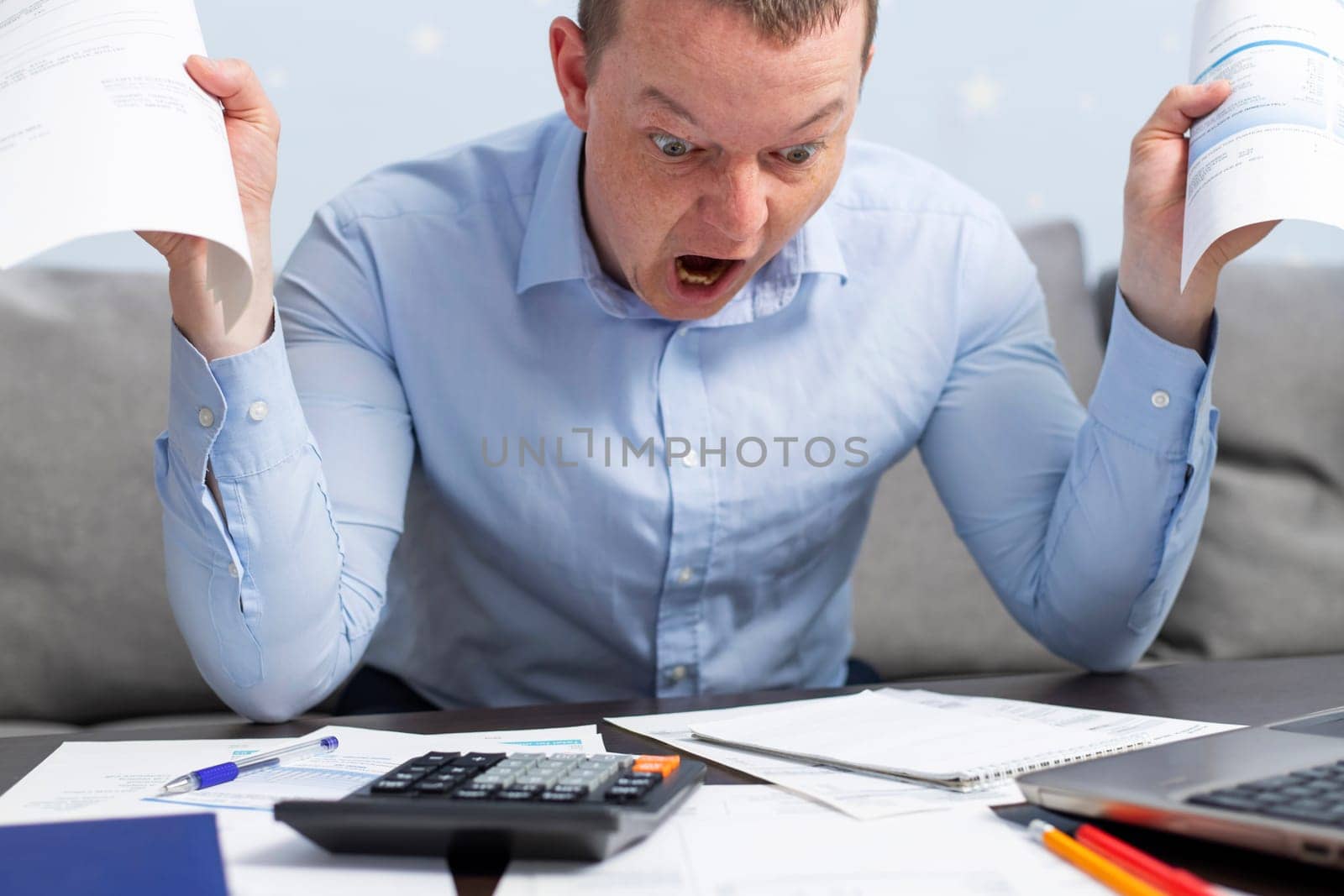 An agitated panicked man using calculator for calculate domestic bills at home, doing paperwork for paying taxes