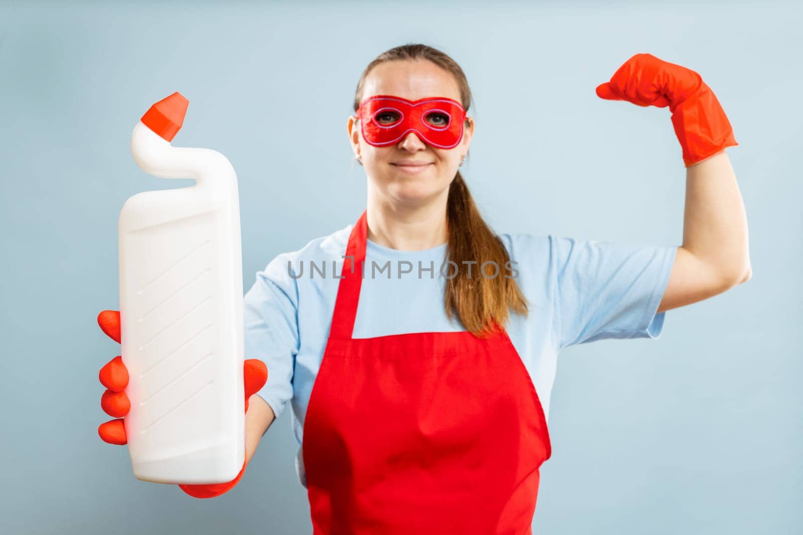 Young woman in red mask, rubber gloves and apron holding cleaning agent bottle. Mockup. Advertising.