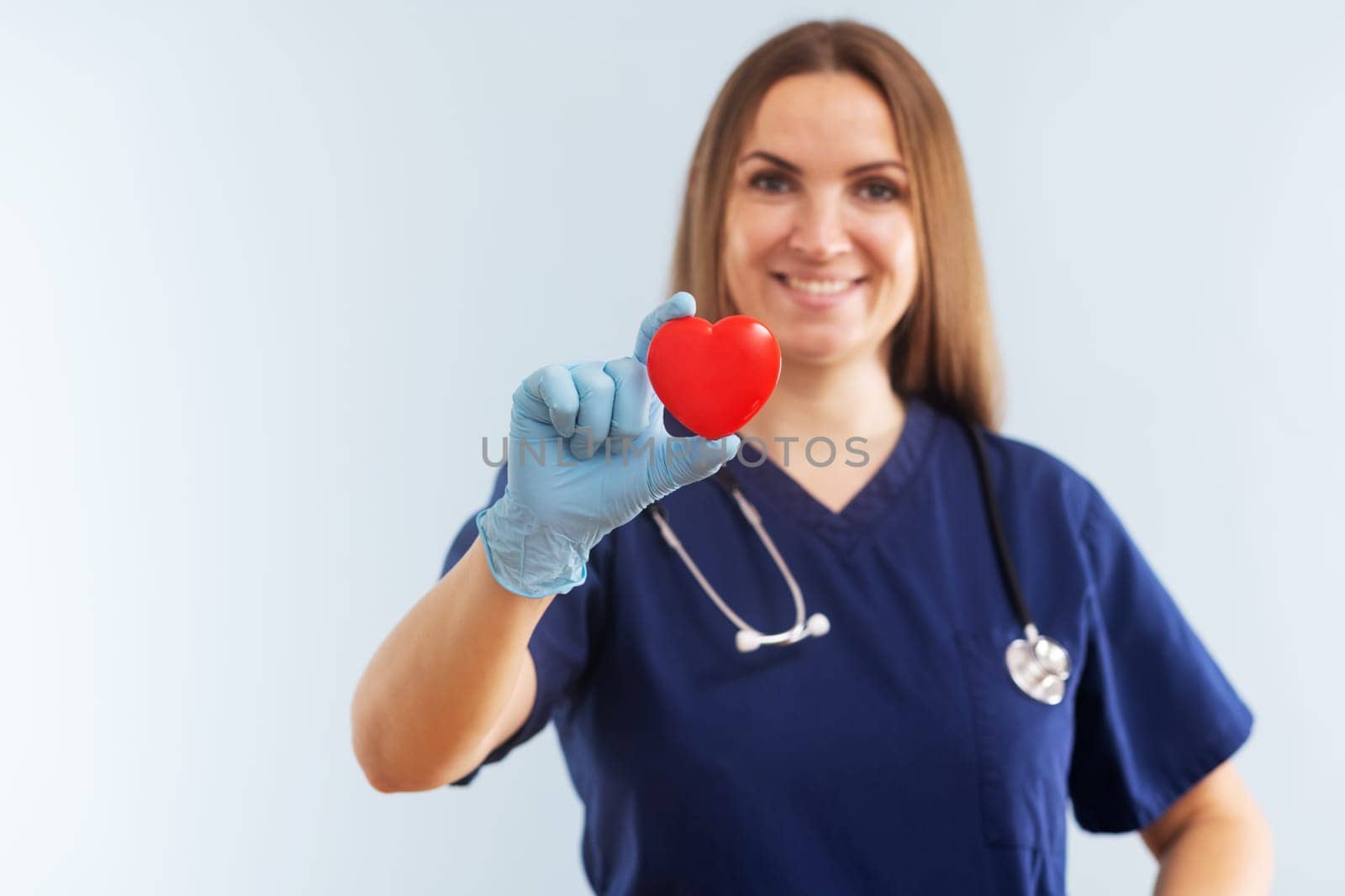 Female doctor in uniform with stethoscope holding red heart on blue background. Healthcare and medical concept