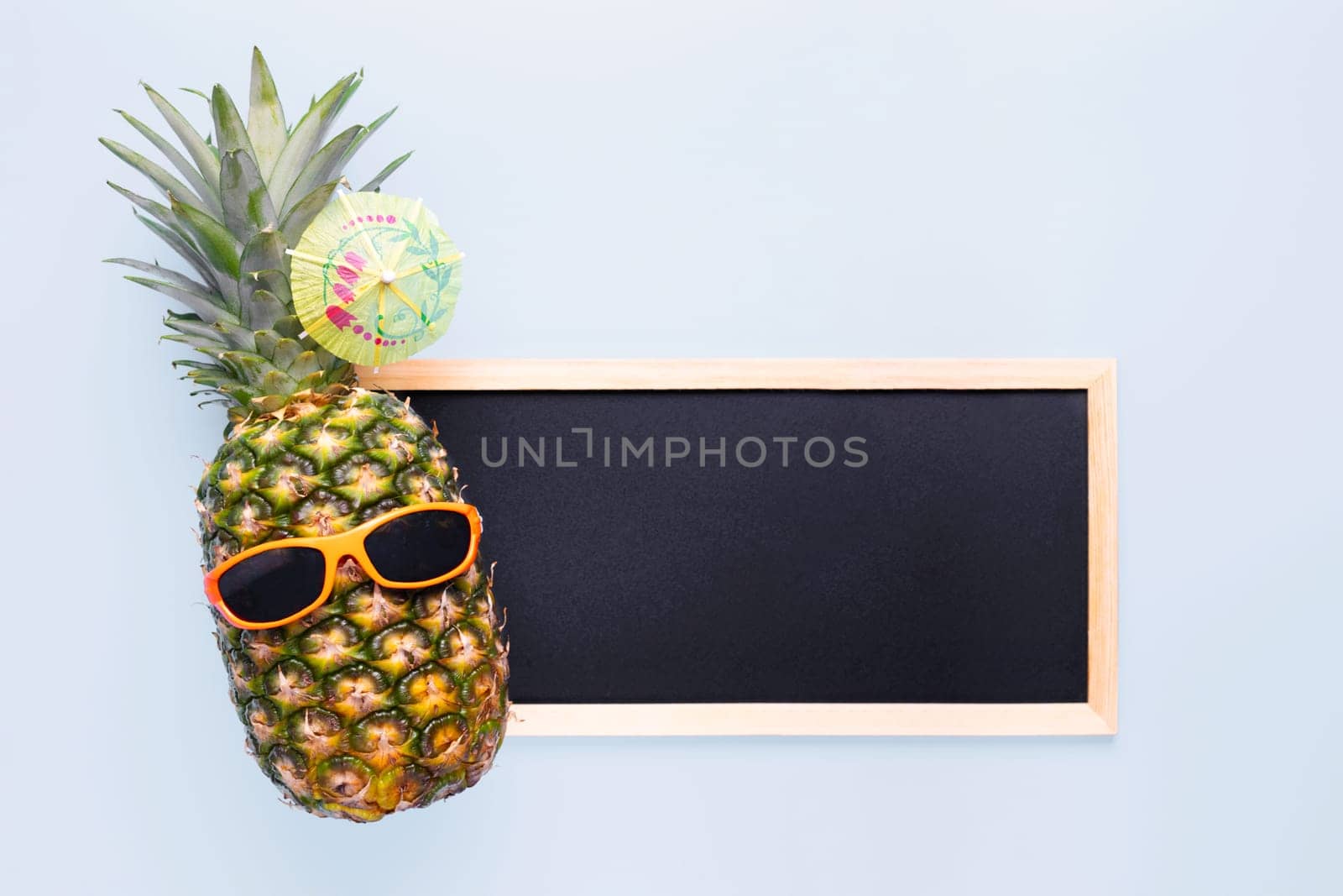 Pineapple in sunglasses with empty copy space blackboard for your text on blue background. Summer vacation party time concept.