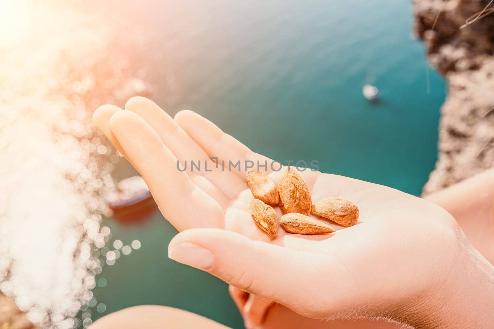 Young milky almond nuts in womans hand. A young caucasian woman eating fresh almond after morning fitness yoga near sea. Only hands are visibly. Healthy vegan food. by panophotograph