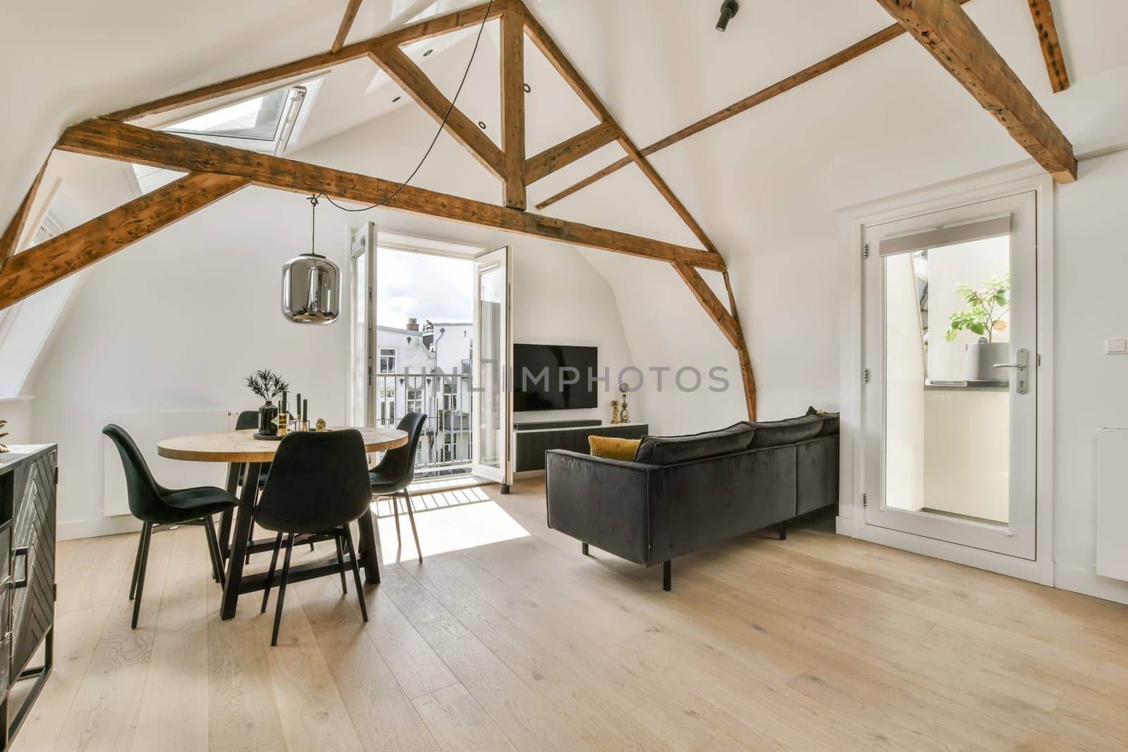 a living room with wood flooring and exposed beams on the ceiling above it is a dining table, two black chairs and a