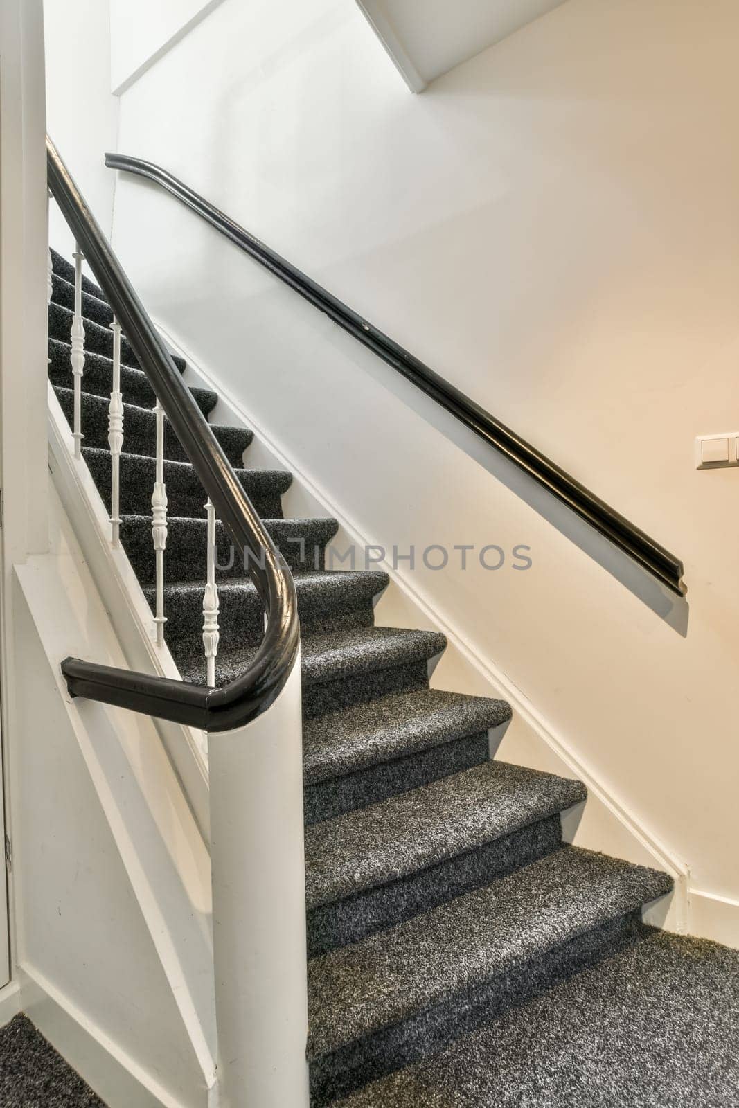 some stairs in a house that is white and has grey carpet on the floor, with black railings leading up to the top