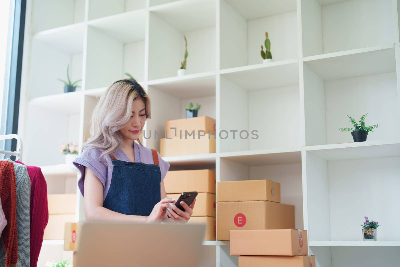 Starting small business entrepreneur of independent Asian female online seller talking on the phone with a customer and packing products for delivery to the customer. and SME delivery concept by Manastrong
