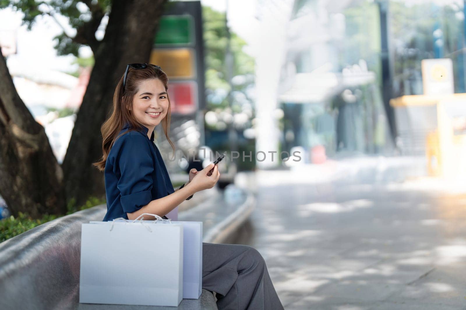 Woman using smartphone holding Black Friday shopping bag while standing on the side with the mall background by nateemee