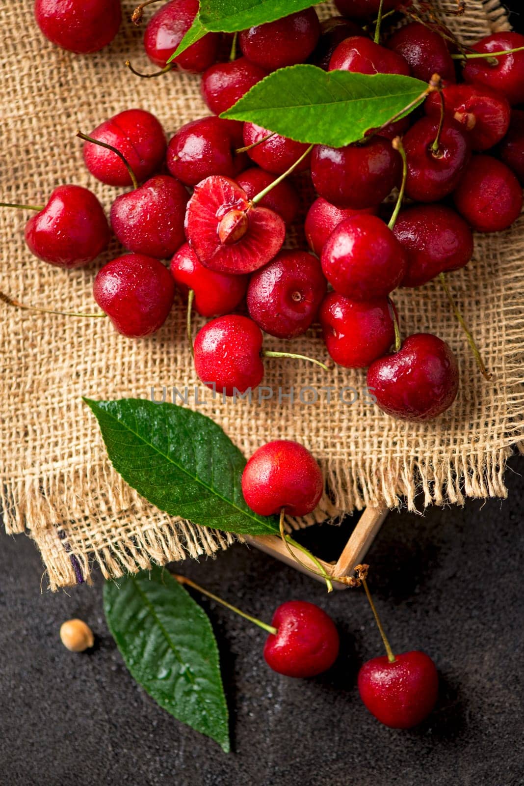 Sweet red cherry on burlap on a black background. A large number of cherries with leaves on the table, on a black background. close-up. by aprilphoto