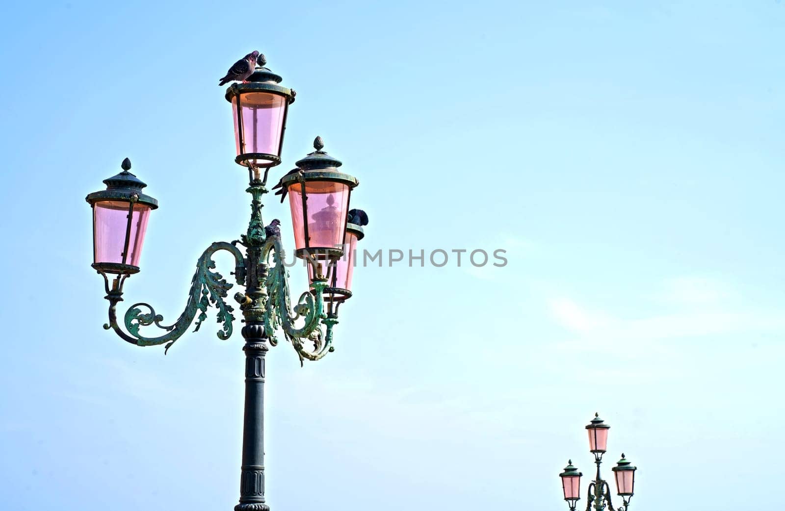 Lantern on the street of Venice. The famous pink lights of Venice. Four lamps with pink glass are on an ornate black metal lamp post. Blue cloudless sky. Nice background, postcard by aprilphoto