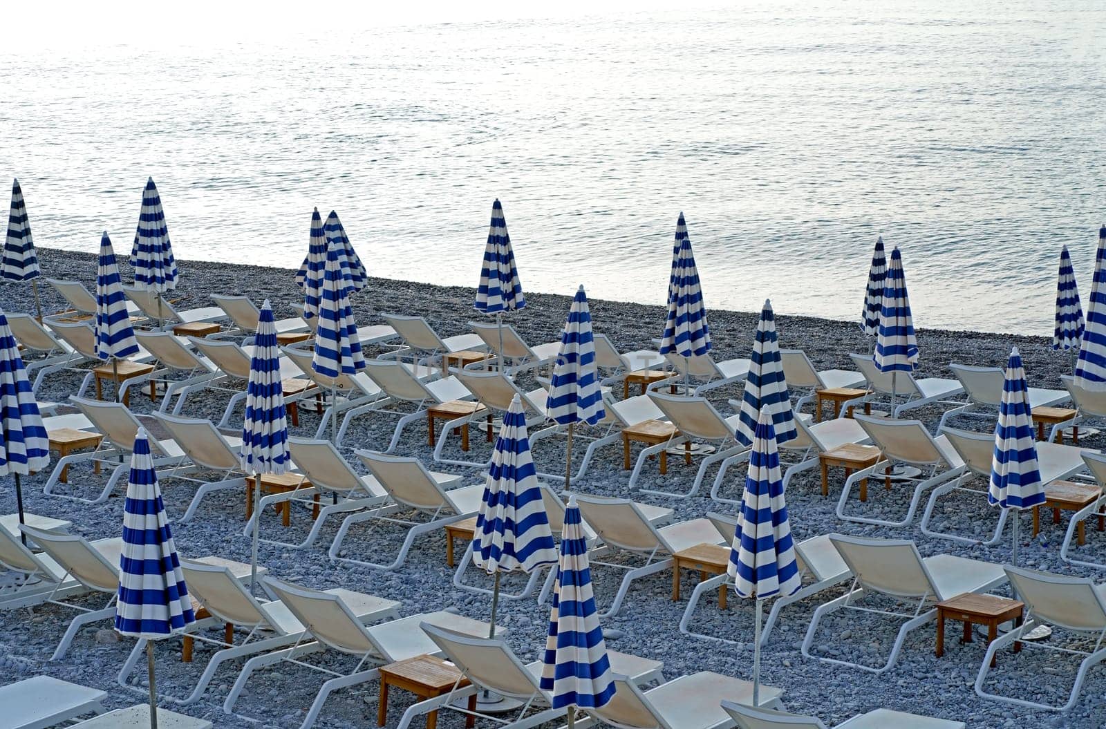 Nice, France - October 2023: View of the beach with sun loungers and collected striped umbrellas in Nice. The beach and the Promenade des Anglais are empty in the winter season. by aprilphoto