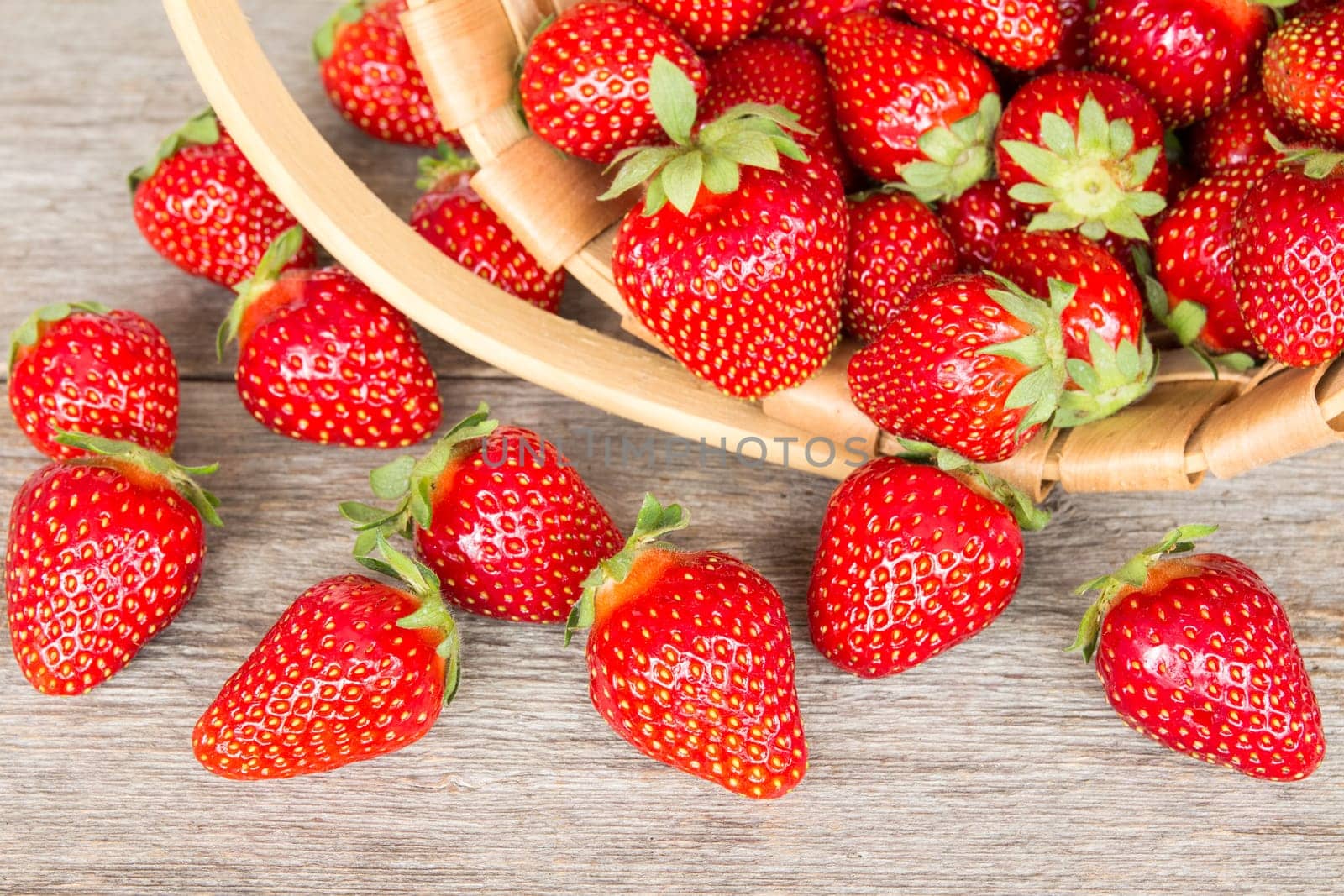 Ripe strawberry in wicker basket on a wooden background
