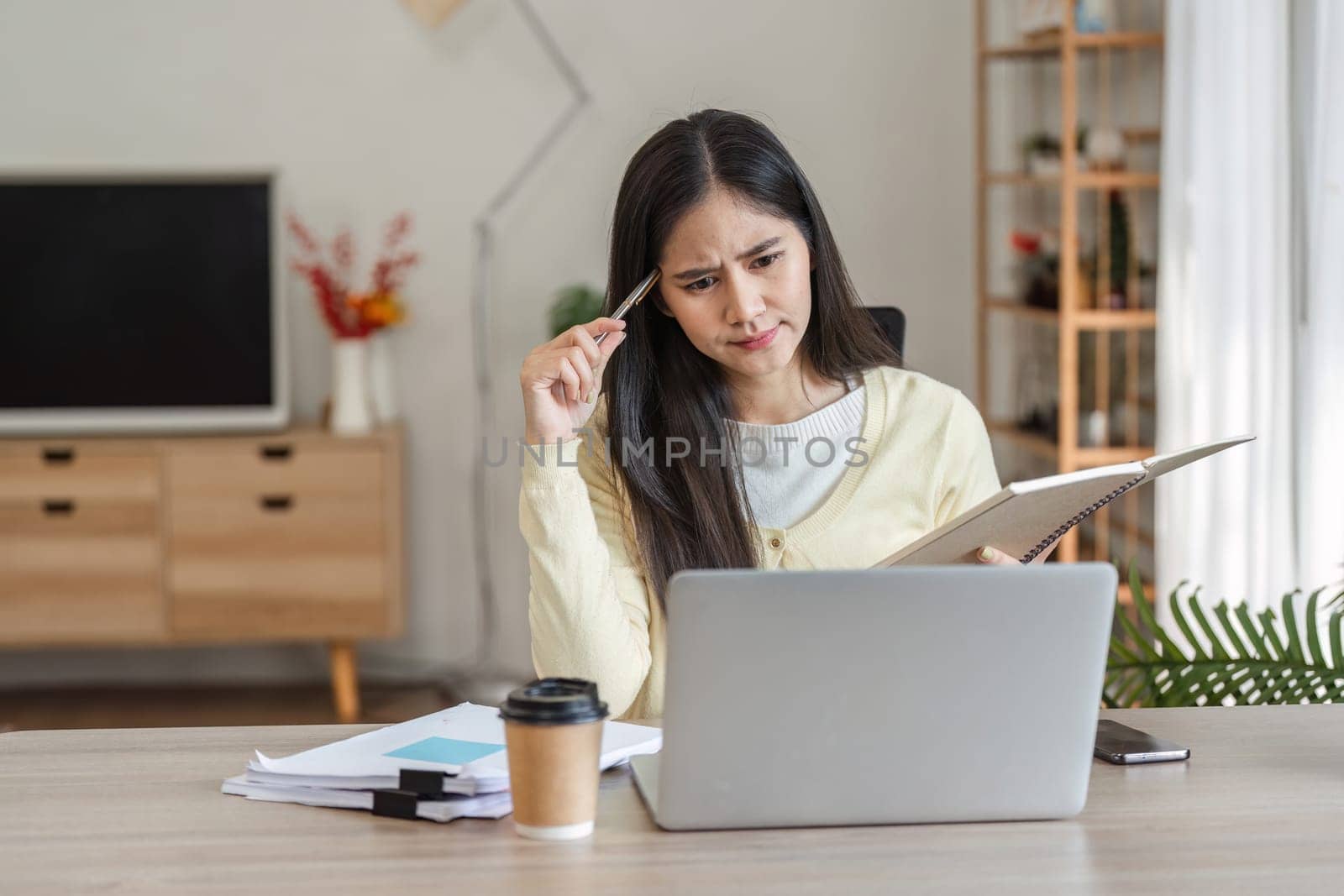 A dedicated businesswoman works from home, concentrating on her freelance projects while managing her tasks with a laptop and notes.
