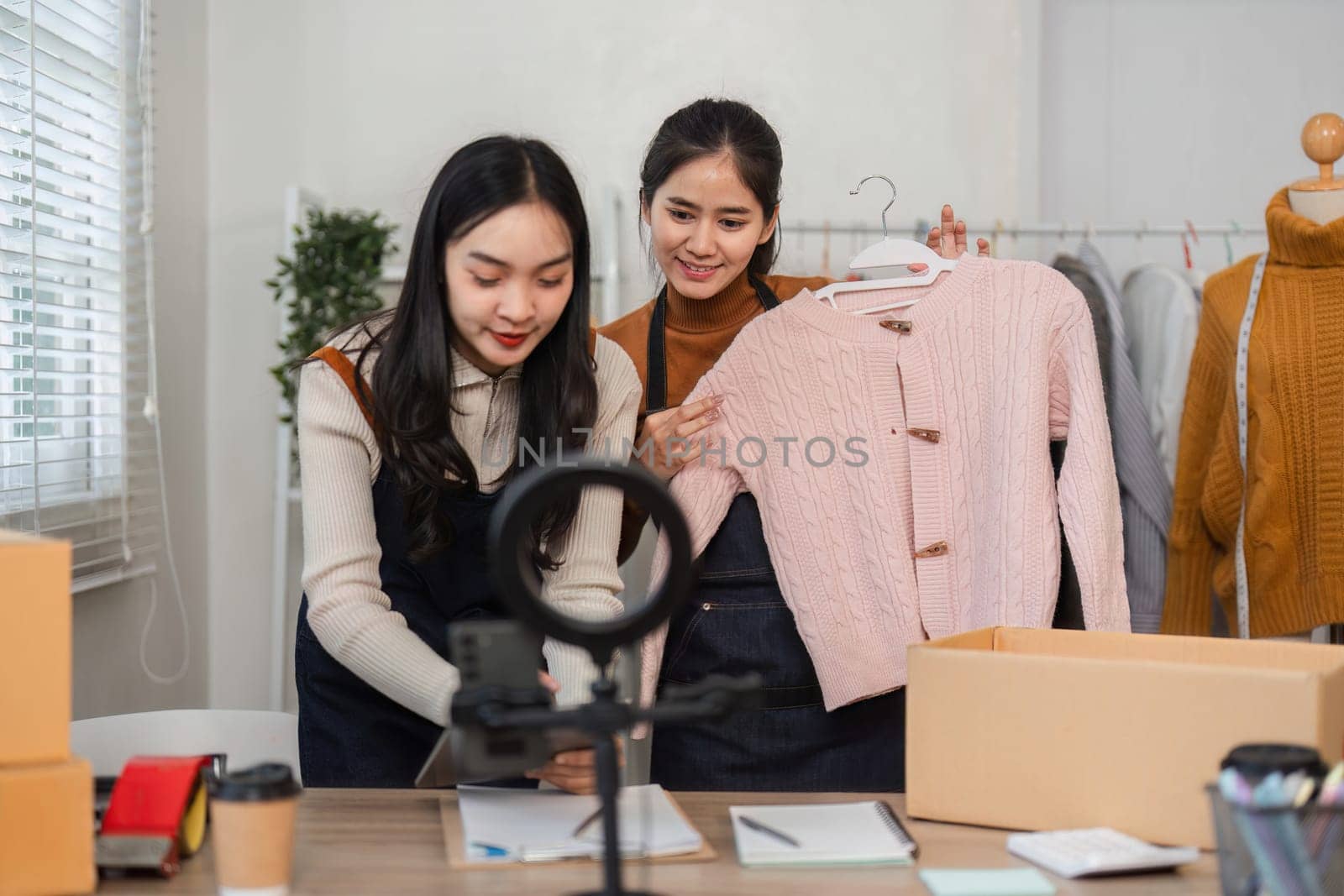 Two women are filming a clothing showcase for online sales, emphasizing teamwork and modern entrepreneurship in fashion.