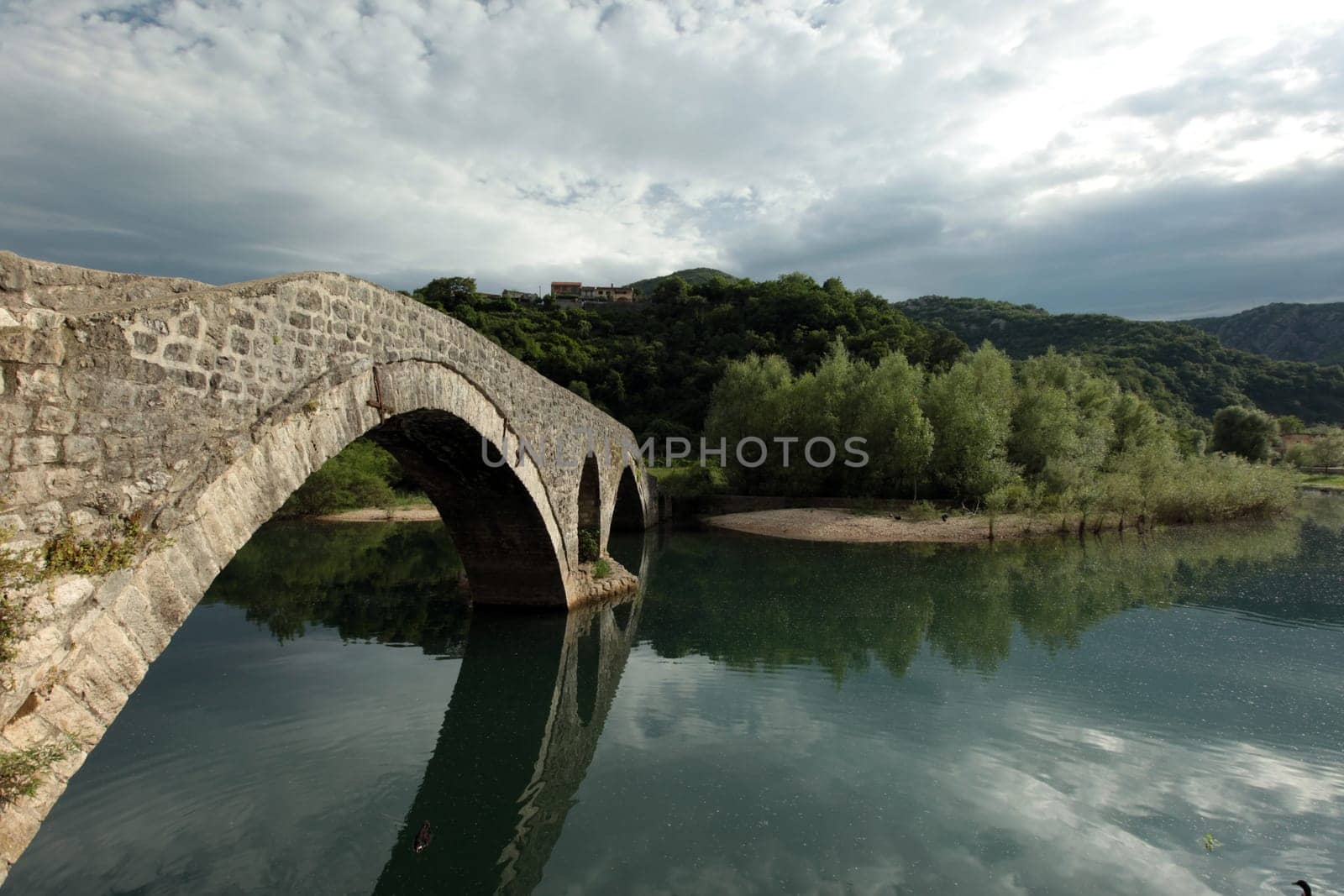 The landscape with the stone bridge of Rijeka Crnojevica with the river Rijeka Crnojevica at the western end of the Skadarsko Jezero lake or Skadar lake in Central Montenegro in Montenegro in the Balkans on the Mediterranean Sea in Europe.