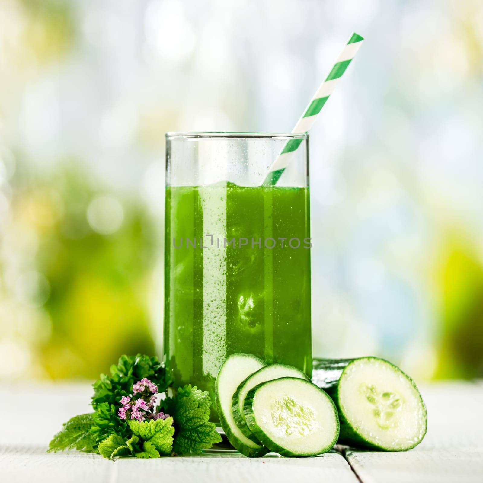 Tasty healthy green vegetable juice with cucumber blended from fresh ingredients and served in a tall glass on a table outdoors in a summer garden