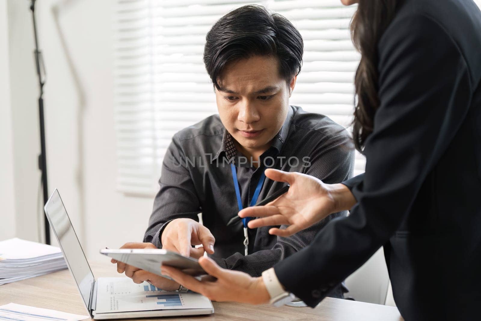 A determined female professional explains complex data to her stressed male colleague, emphasizing teamwork in problem-solving.