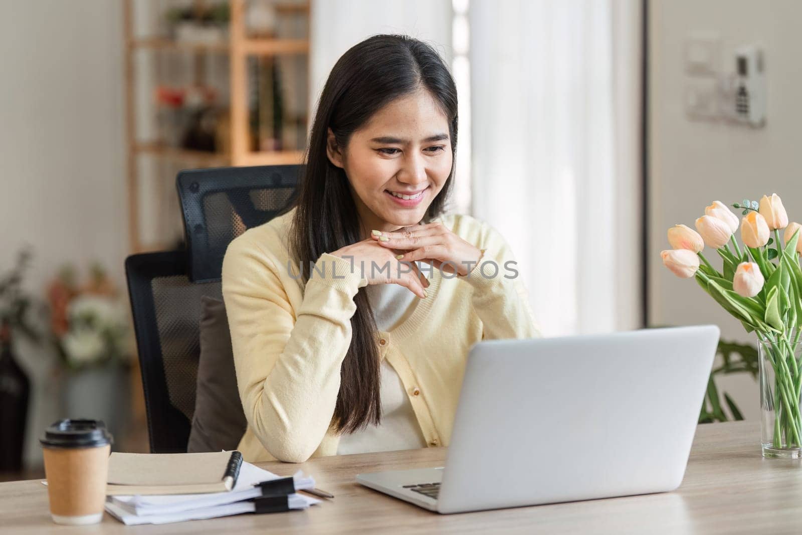 A dedicated freelance businesswoman interacts with clients on her laptop at home, embodying professionalism and commitment.