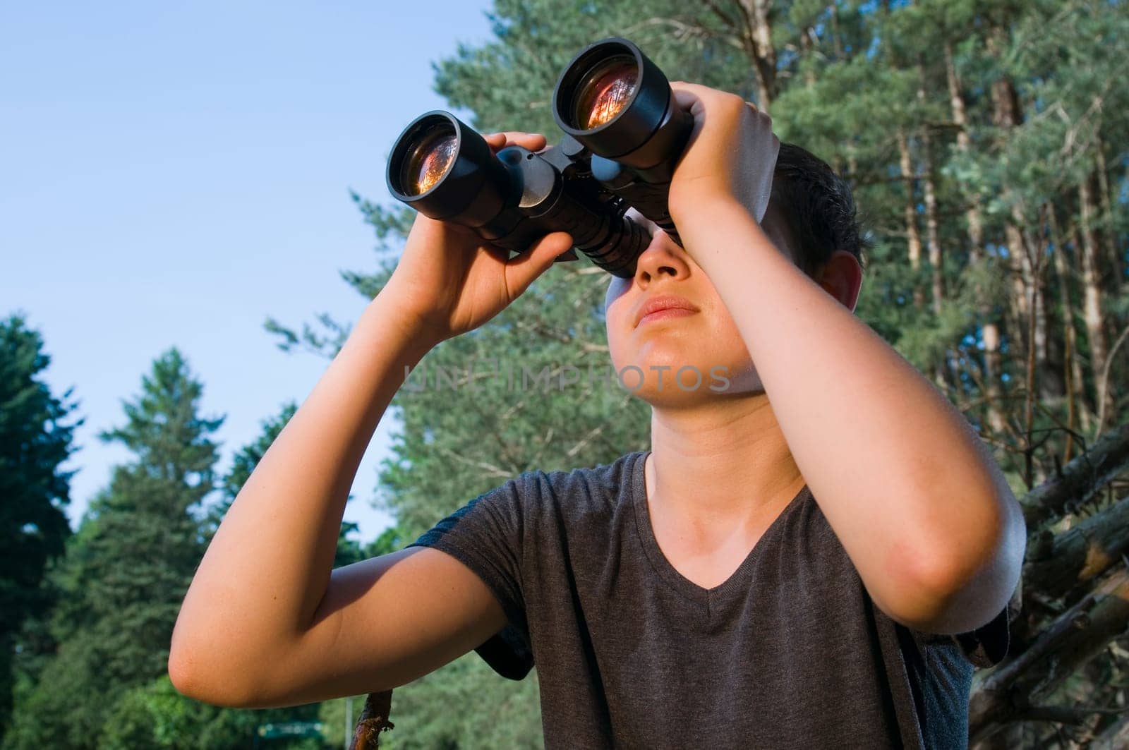 Side head-and-shoulder view of a 13-year-old male teenager looking through binoculars in the woods