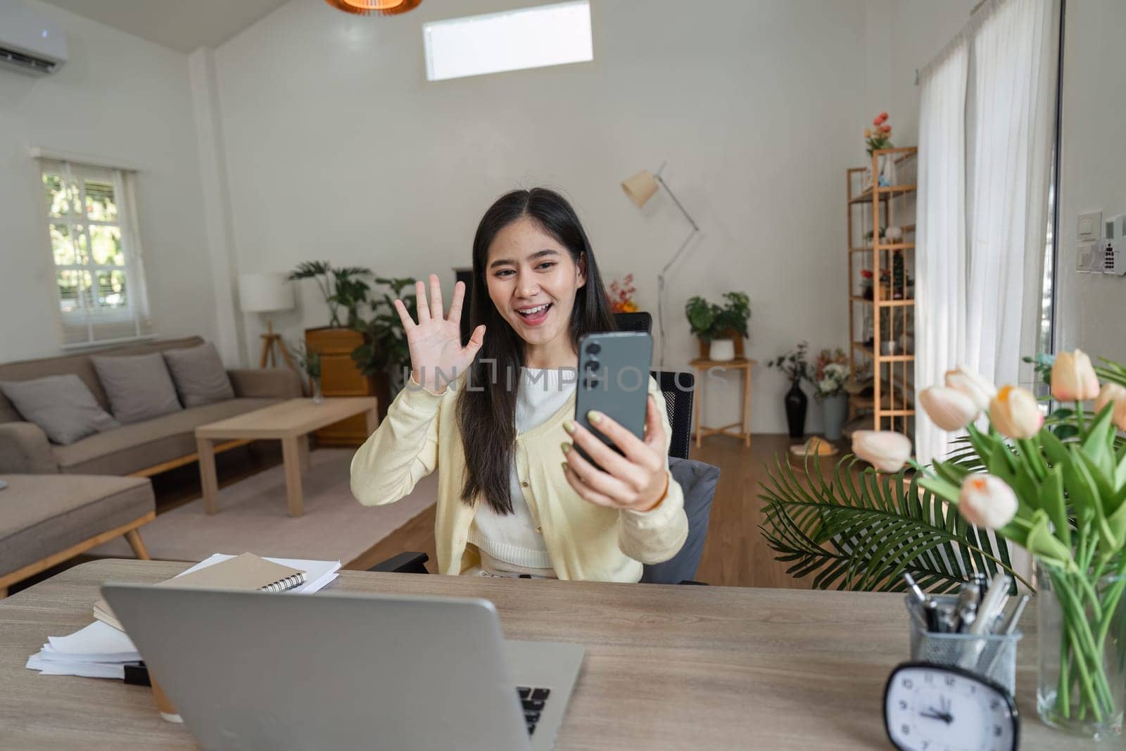 A cheerful young woman participates in a video call from her home office, showcasing a friendly and engaging demeanor.