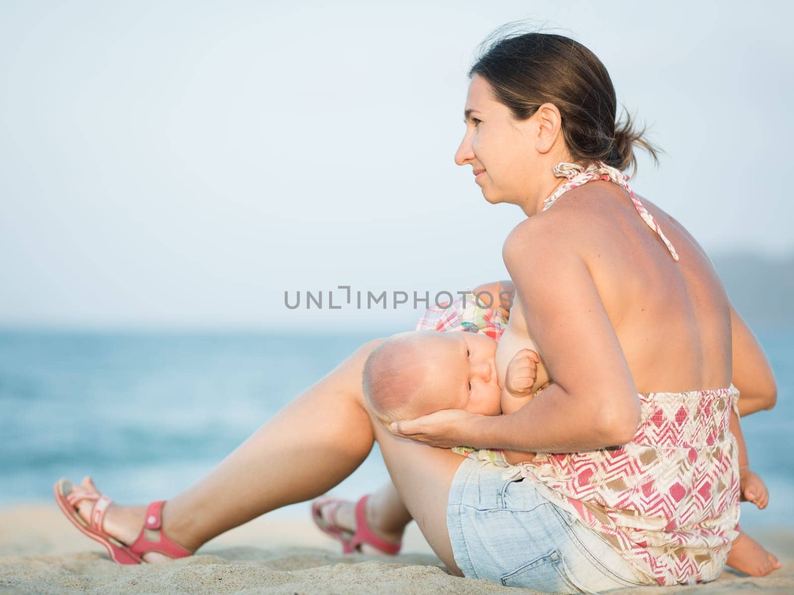 Mother breastfeeding baby on the beach