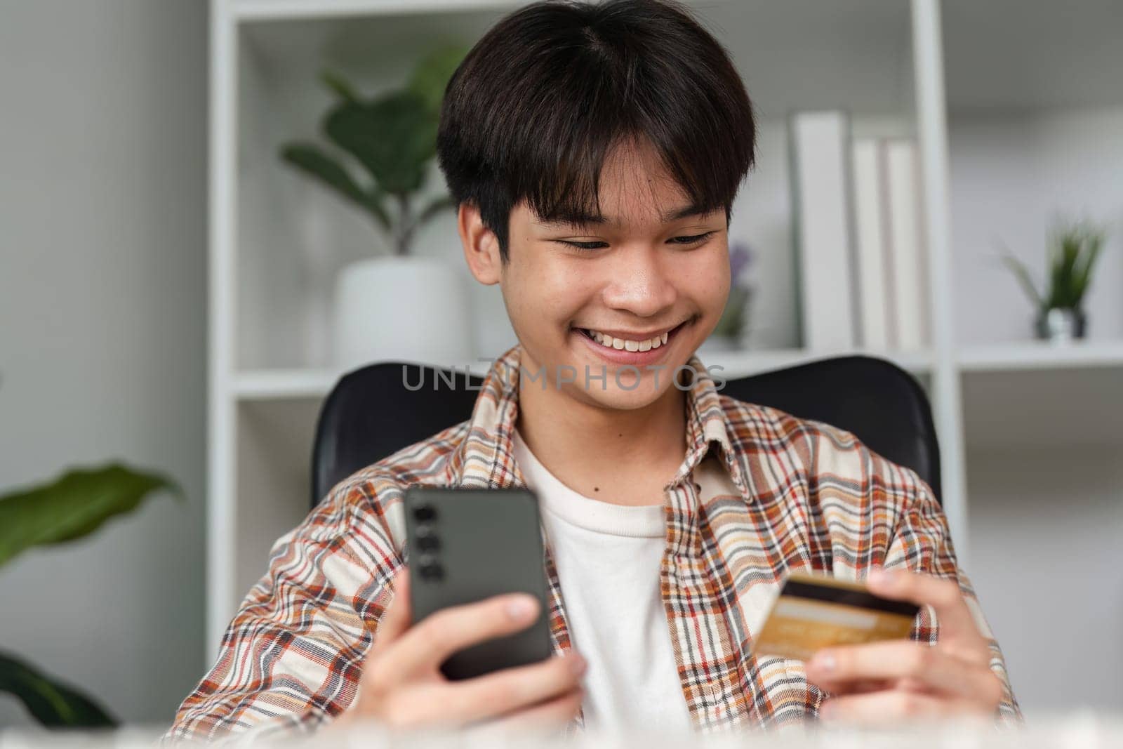 A young adult expresses excitement while managing a financial transaction using a smartphone and credit card.