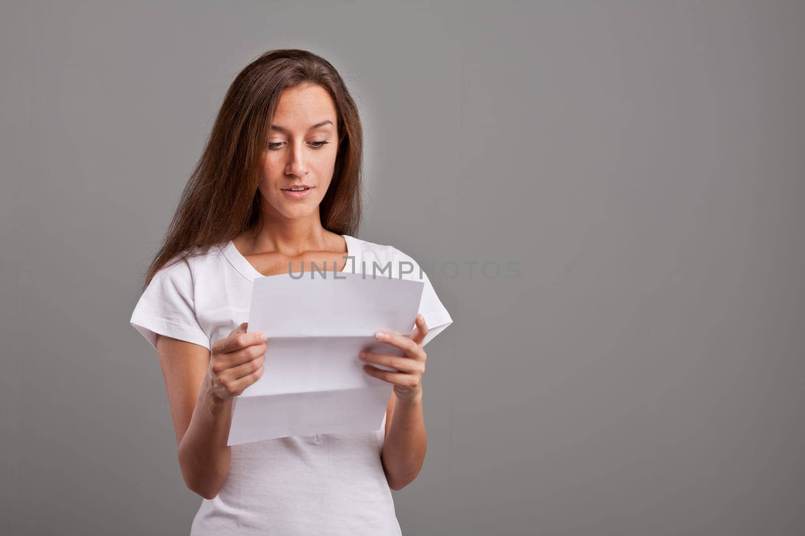 brunette young woman realizes that something GOOD happened reading a white letter or document