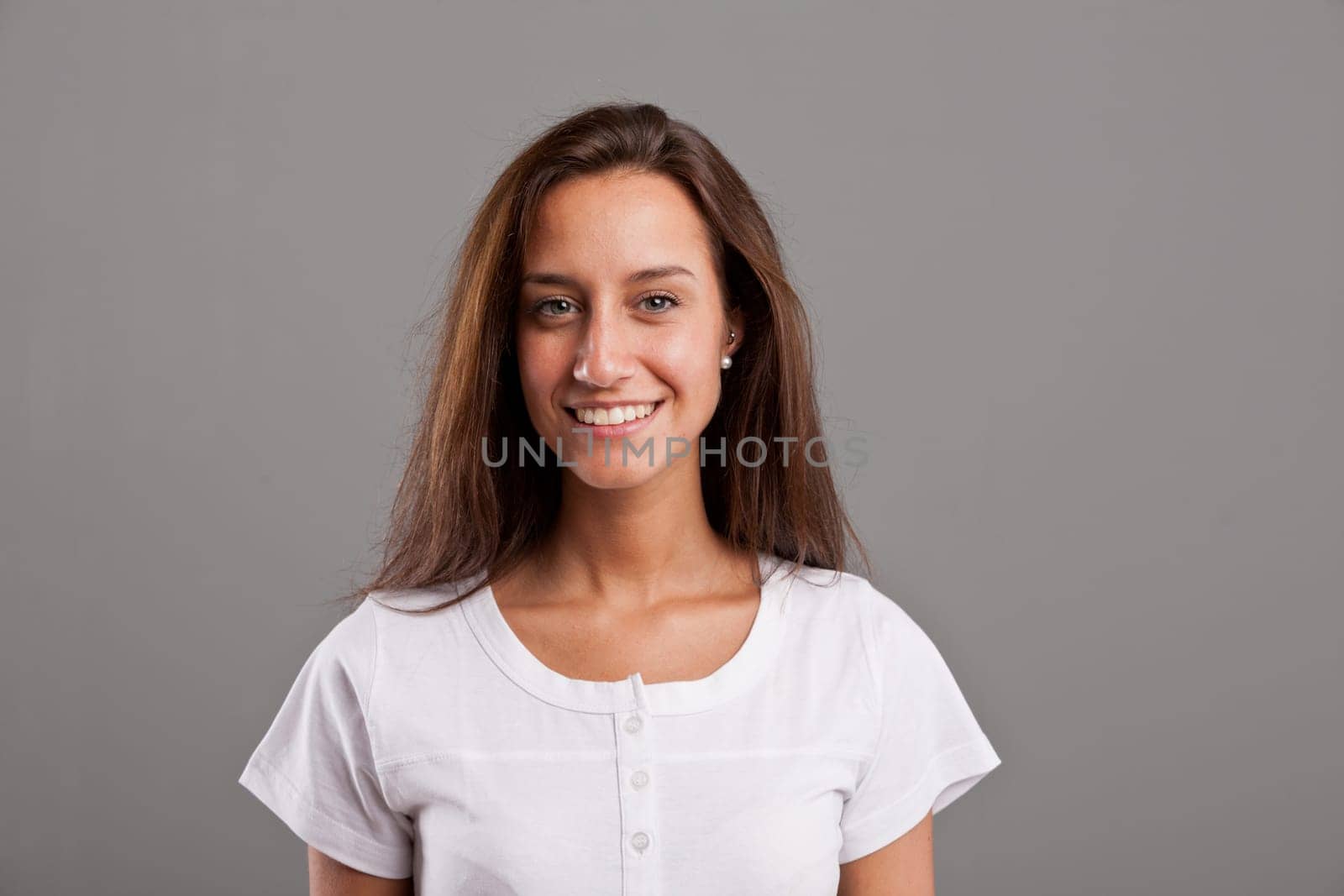 horizontal portrait of a young simple woman smiling sincerely and watching at camera, on a grey neutral background