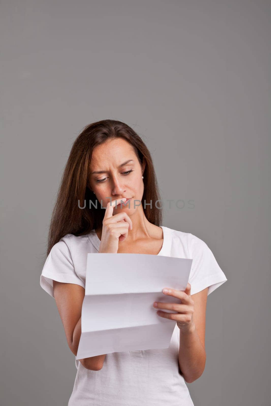 brunette girl reading uncertain news on a white document on a neutral gray faded background