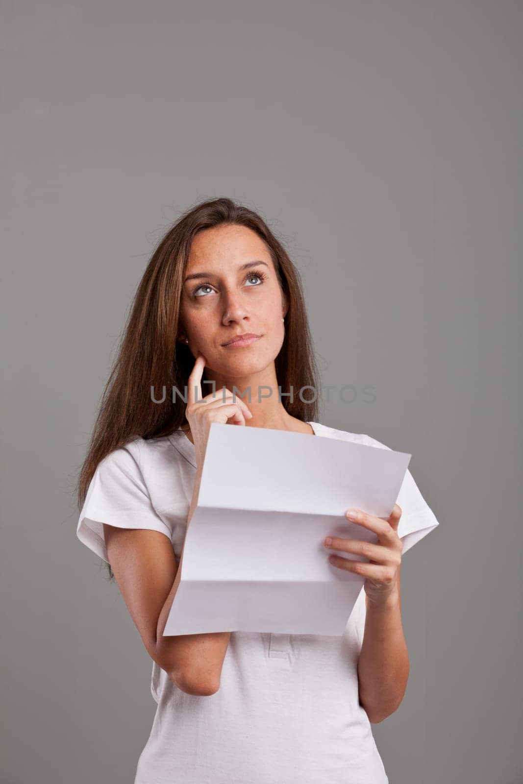 brunette girl thinking about news she received on a white document on a neutral gray faded background