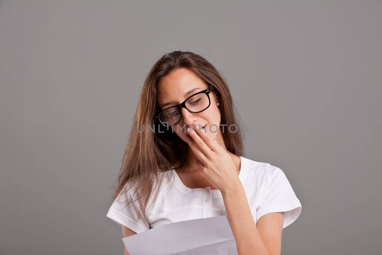 brunette young woman with glasses realizes that someone loves her reading a white letter or document