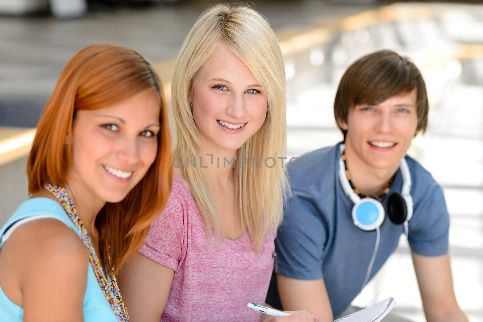 Three smiling college student friends sitting together looking at camera