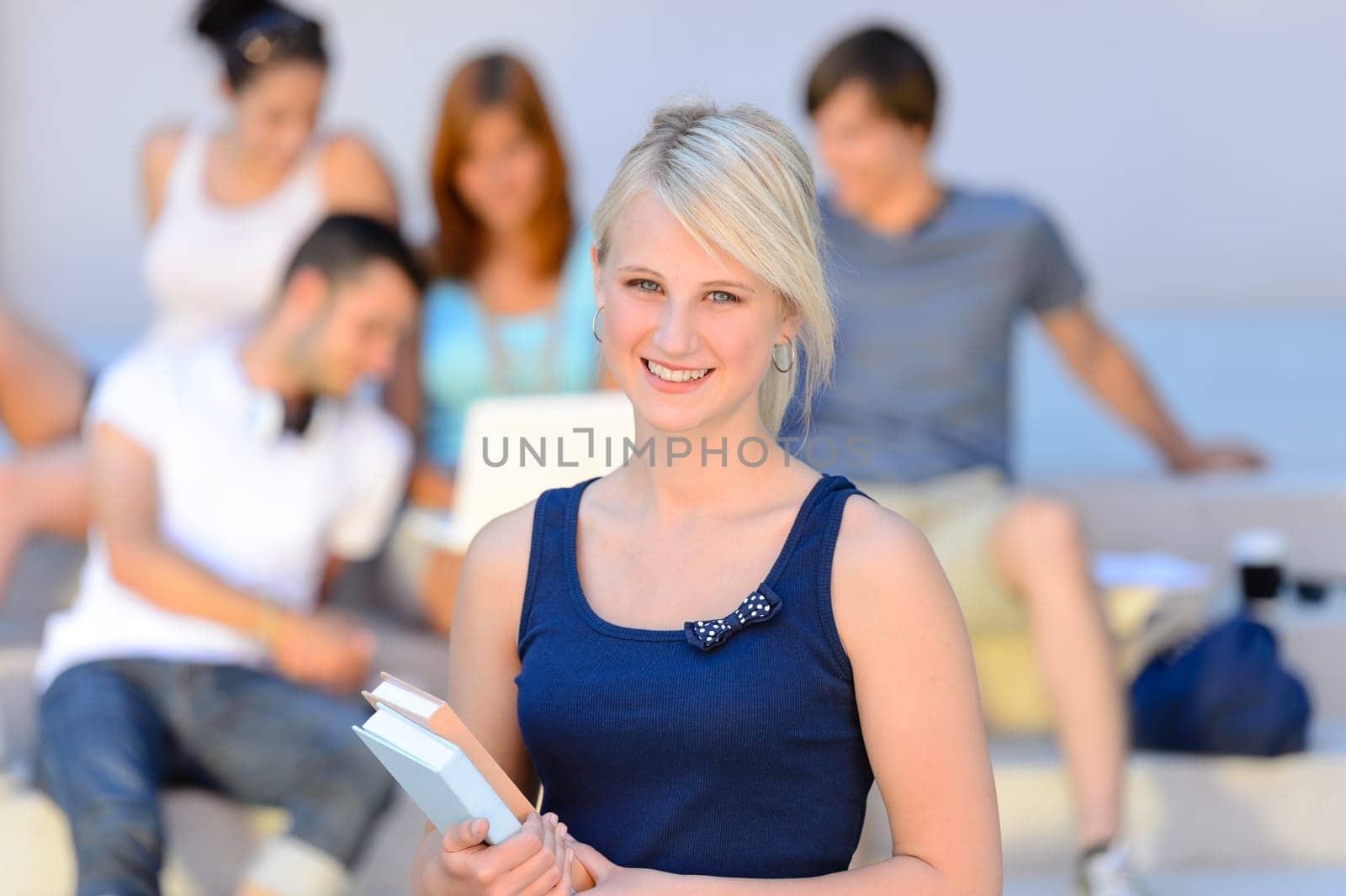 Teenage student girl smiling holding books friends in background summer