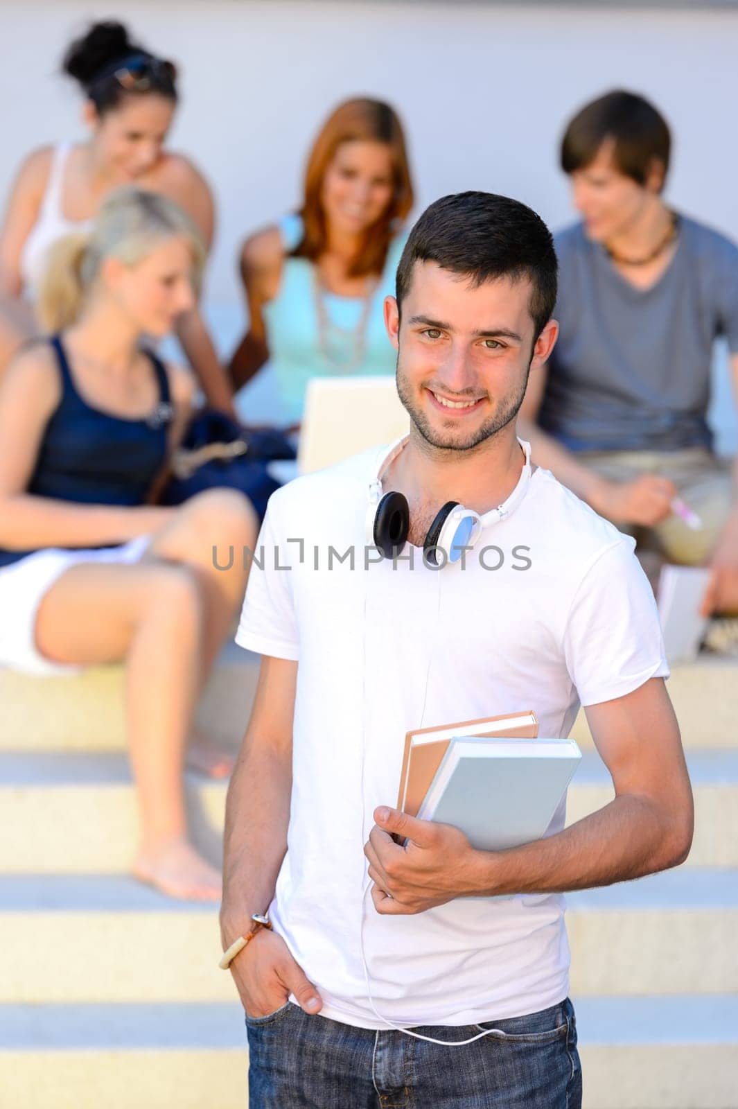 Smiling student boy  holding books friends sitting on college steps