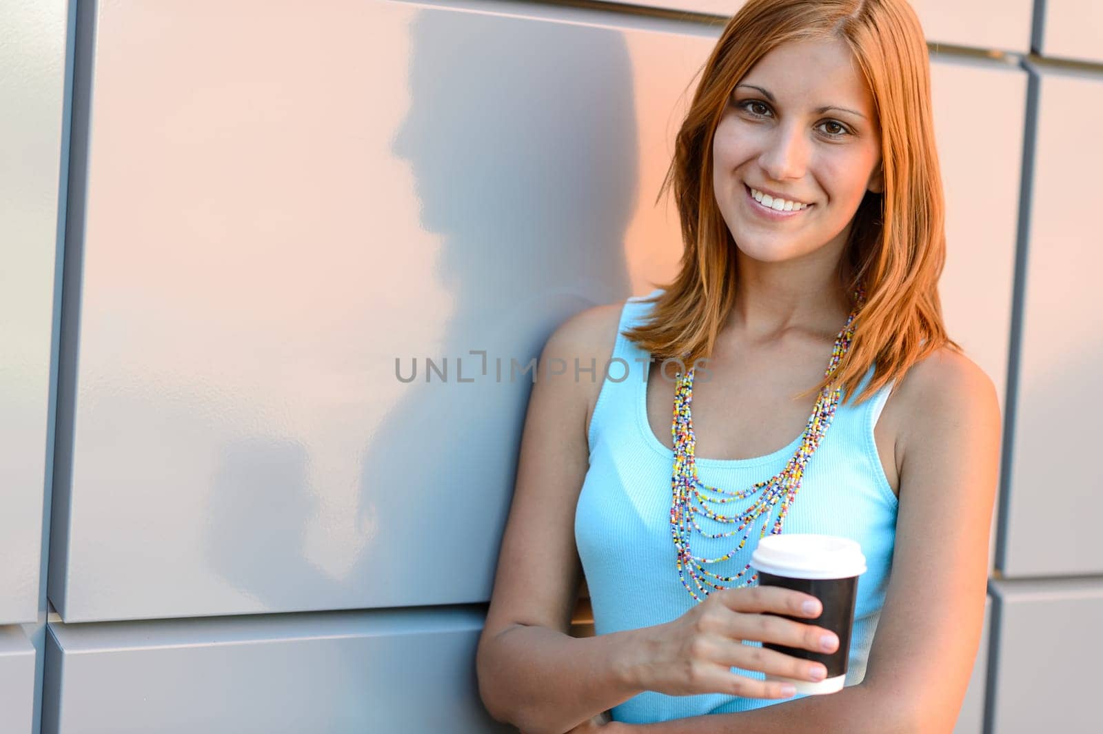Smiling student girl with coffee cup summer standing by wall