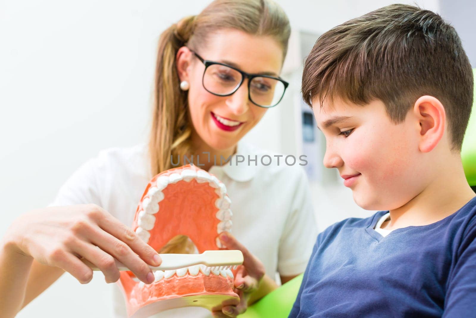 Female dentist explaining boy cleaning tooth with toothbrush on model