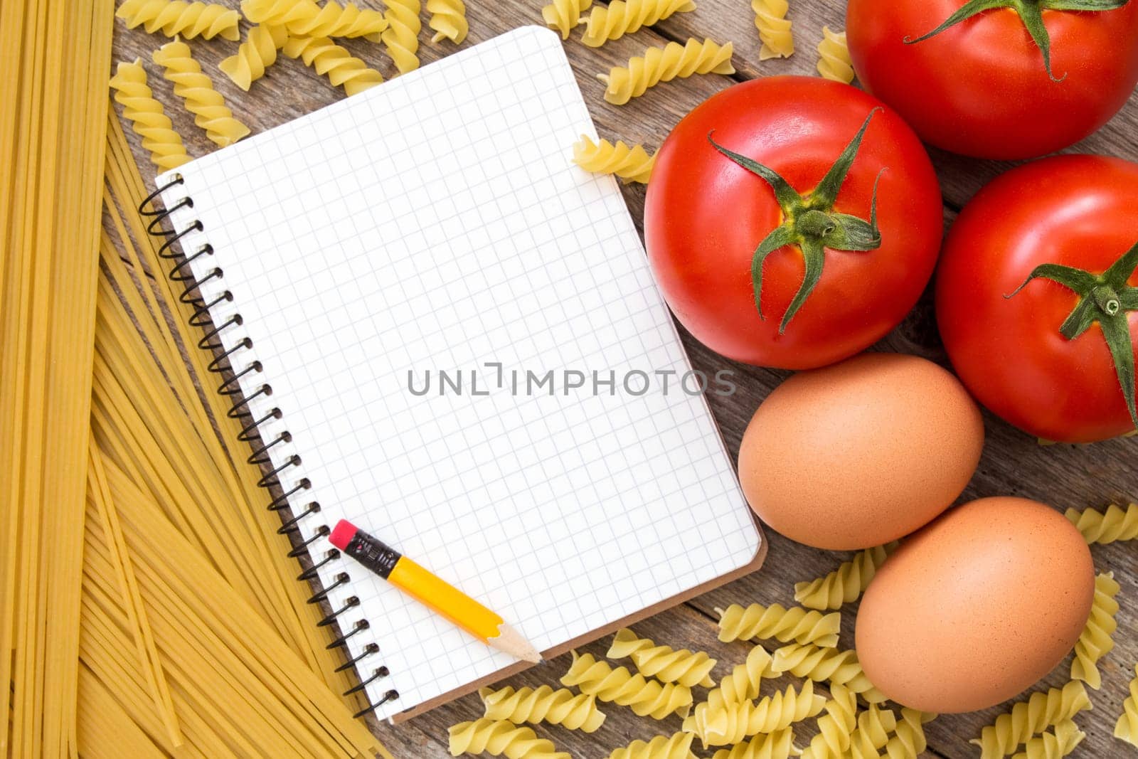 Tomatoes, eggs, uncooked pasta and blank recipe book