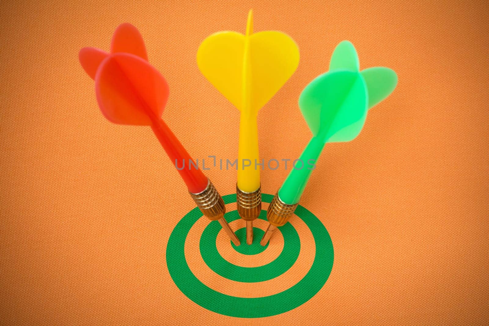 Three darts hitting green target on orange background