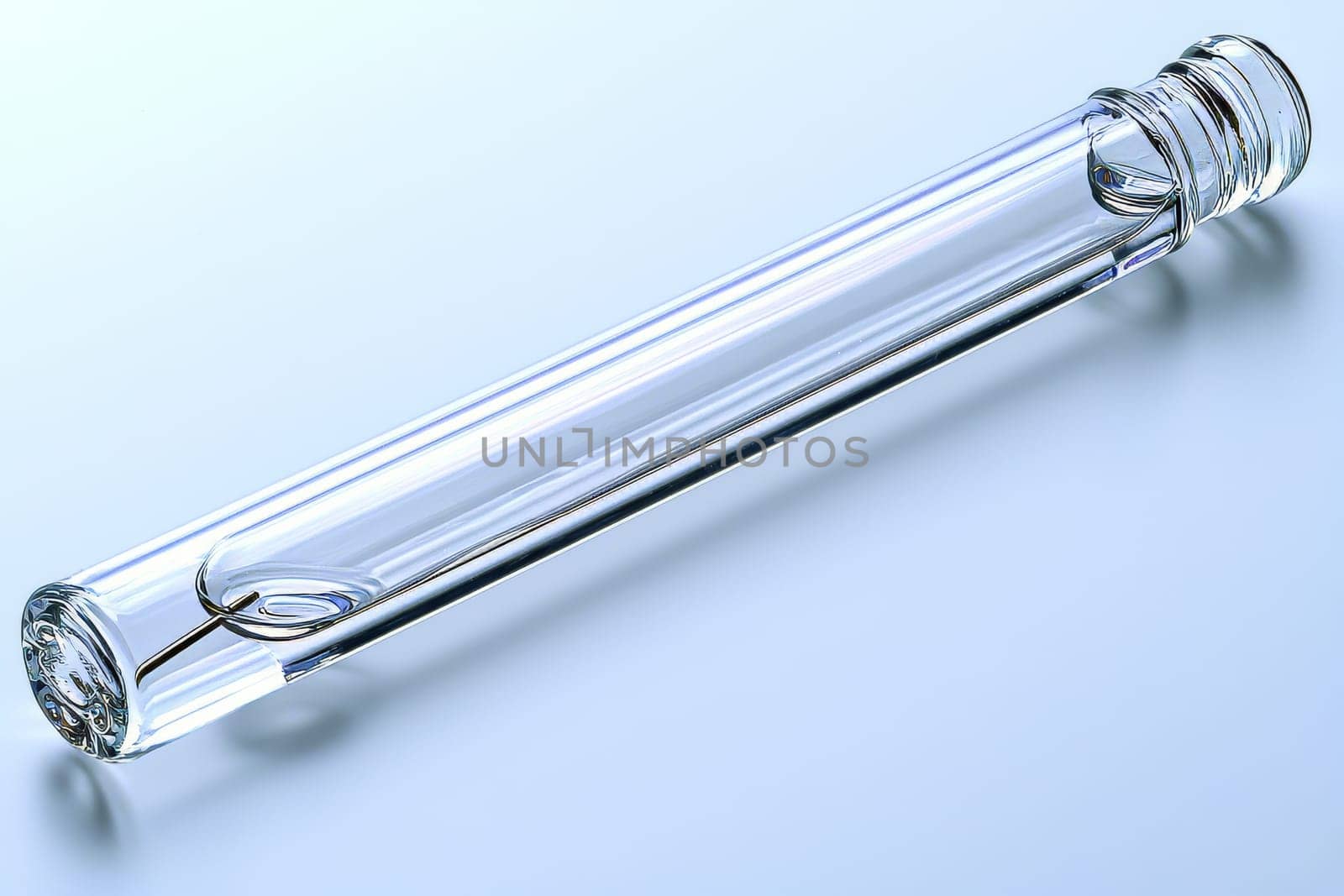 A clear glass tube lies on a reflective surface, highlighting its elongated design and smooth edges under soft lighting.