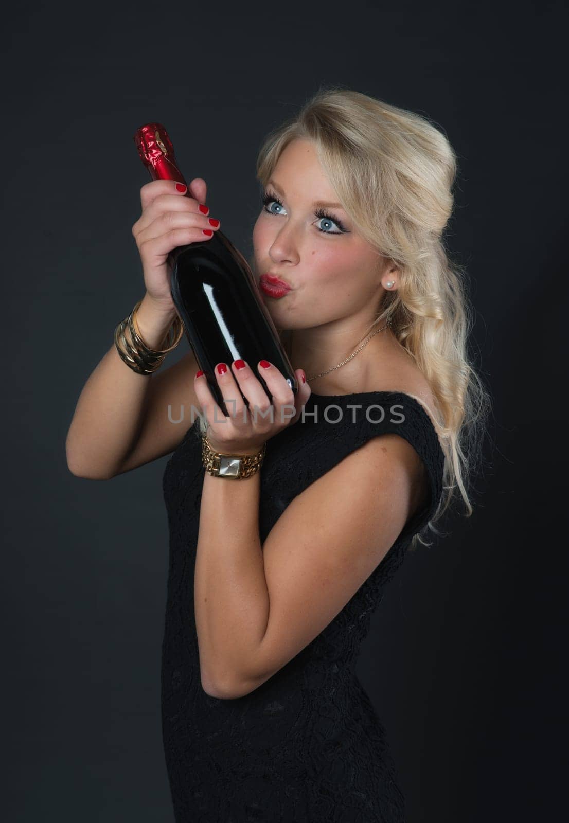 Beautiful blonde woman kisses red wine bottle