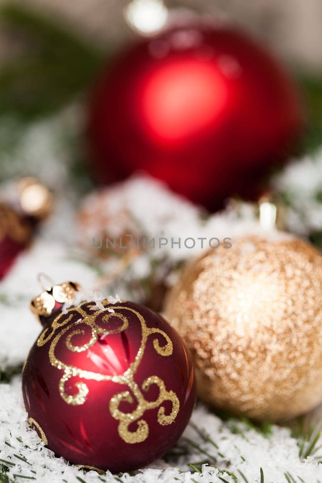 red Christmas baubles between cones and fir branches covered with snow as macro detail