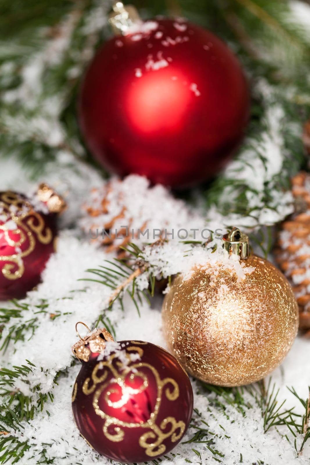 red Christmas baubles between cones and fir branches covered with snow as macro detail