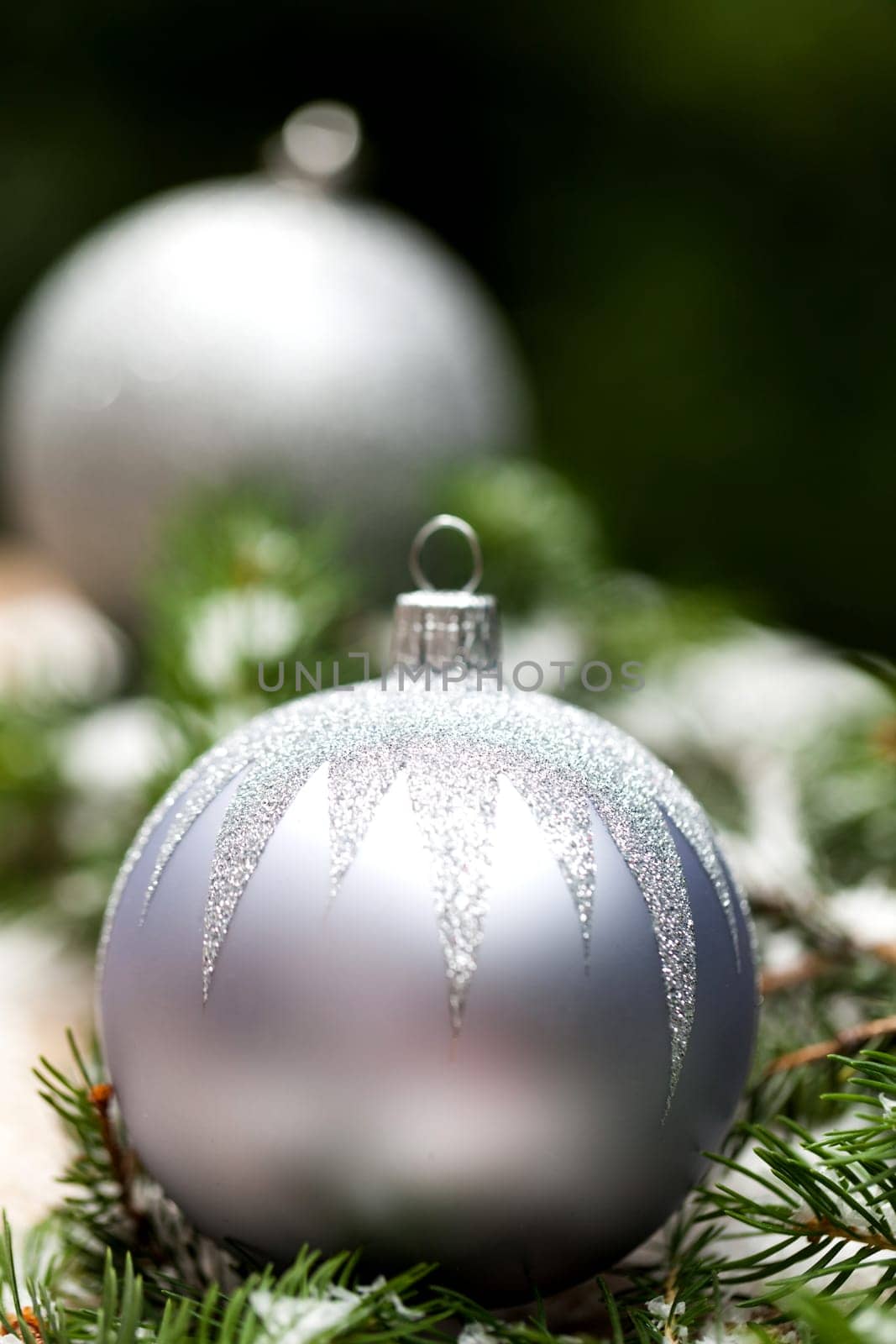Silver Christmas tree balls in green fir branches with white shiny snow as macro detail