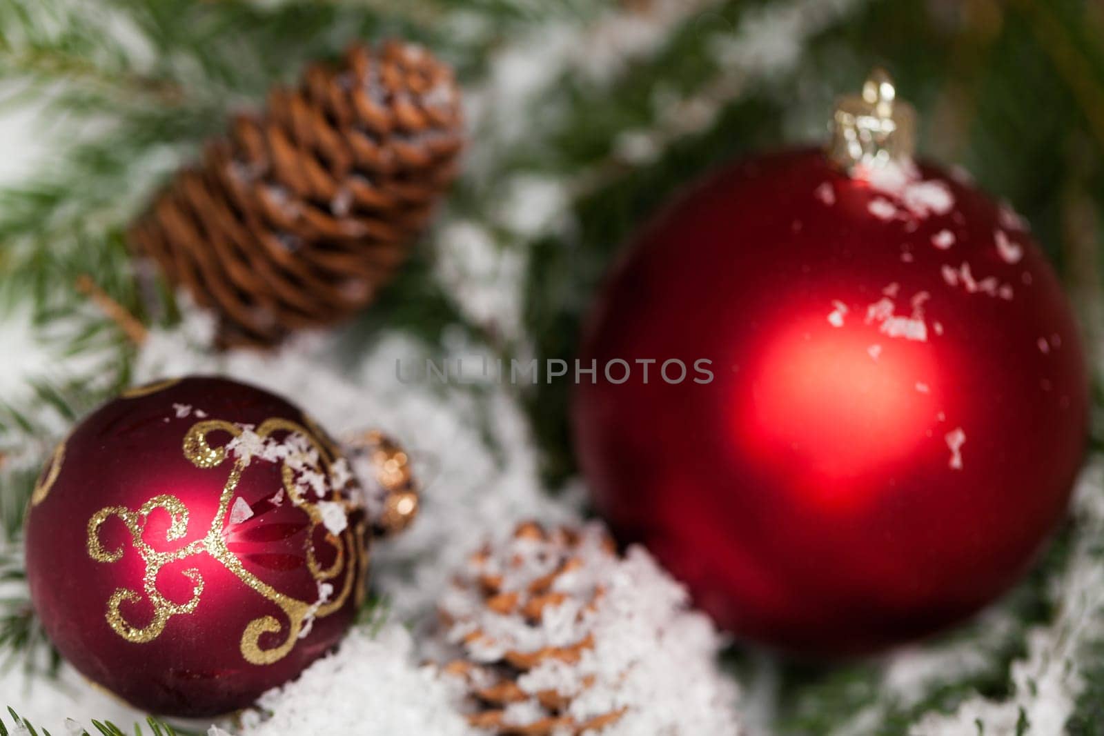 red Christmas baubles between cones and fir branches covered with snow as macro detail