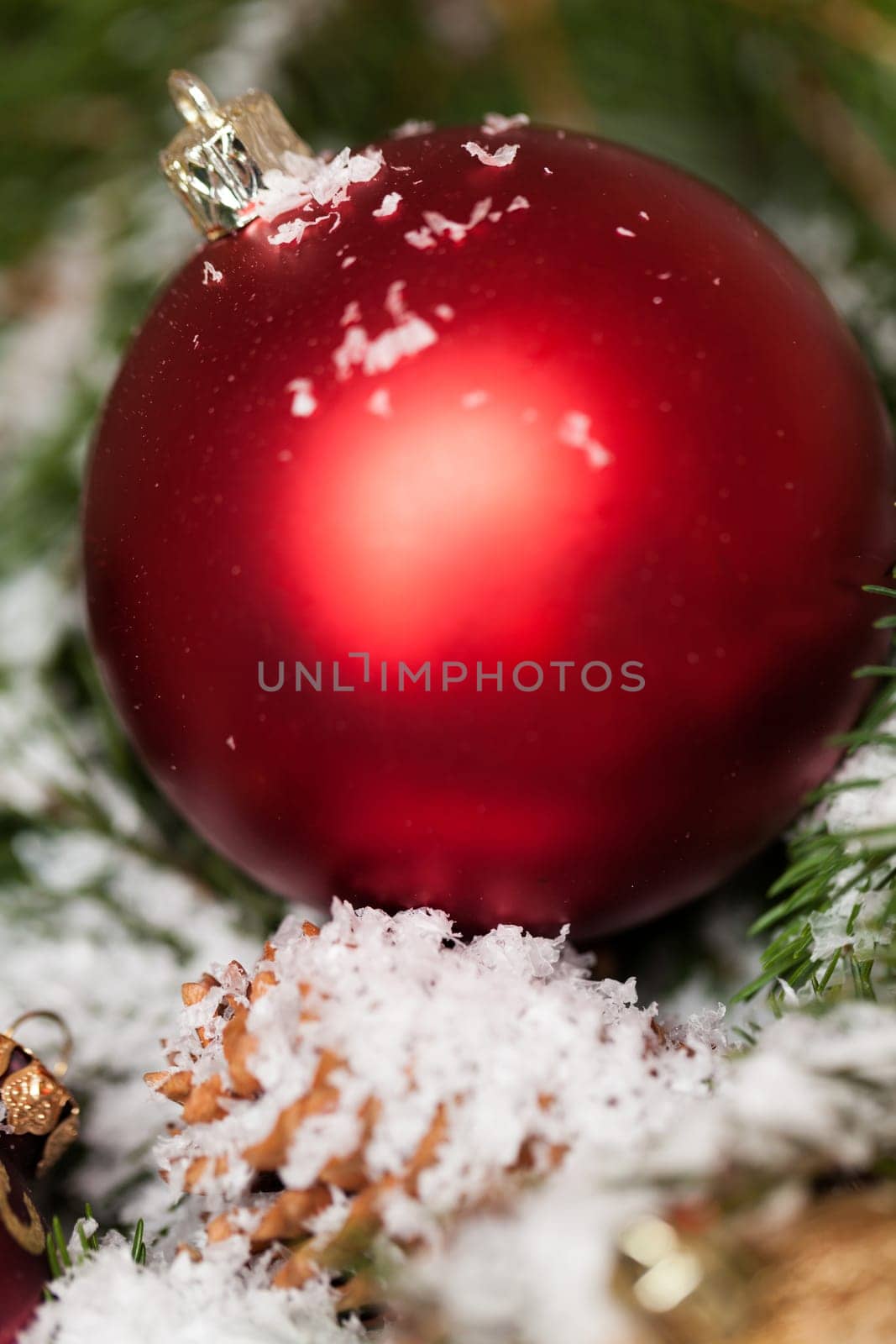 red Christmas baubles between cones and fir branches covered with snow as macro detail