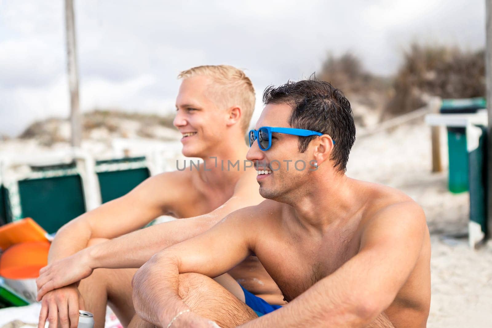 Two young men friends relax in the sand while on holiday on the beach in summer