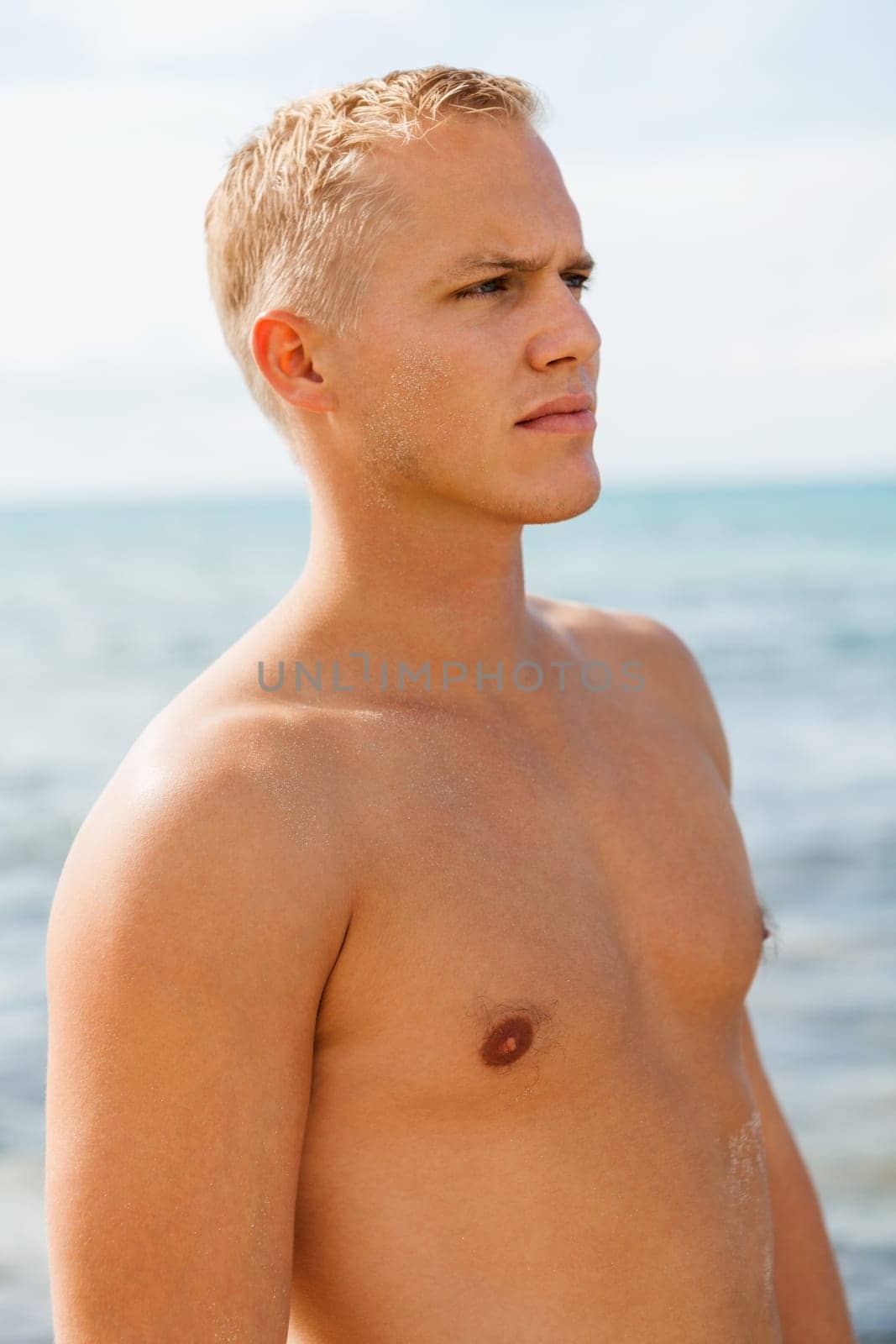 Young man in blue swimming trunks stands on the beach in the blue sea on holiday