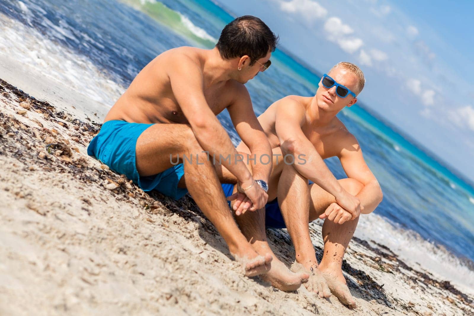 Two young men friends relax in the sand while on holiday on the beach in summer